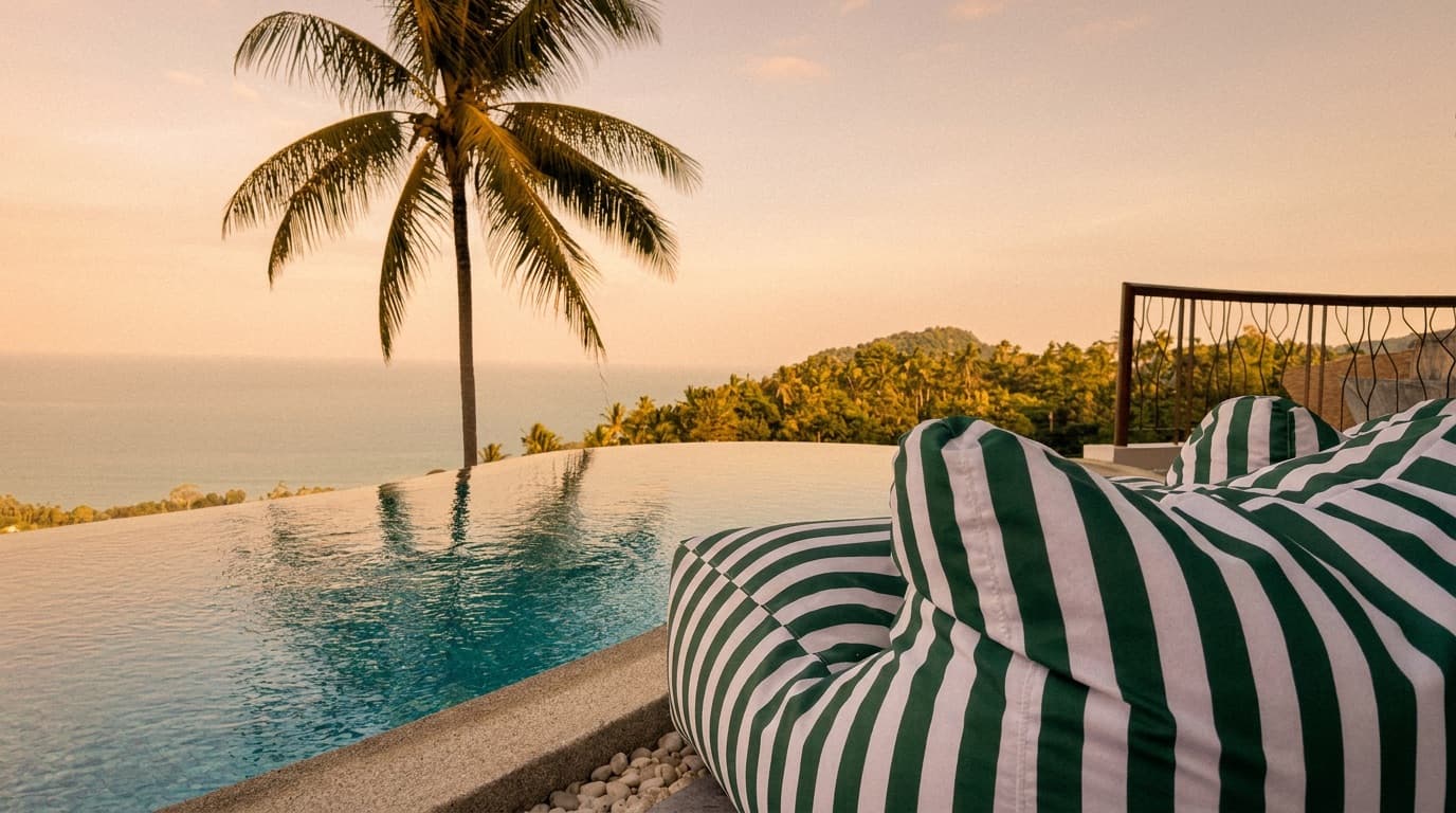A sun lounger beside the infinity pool, looking past a palm over the forest to the sea.