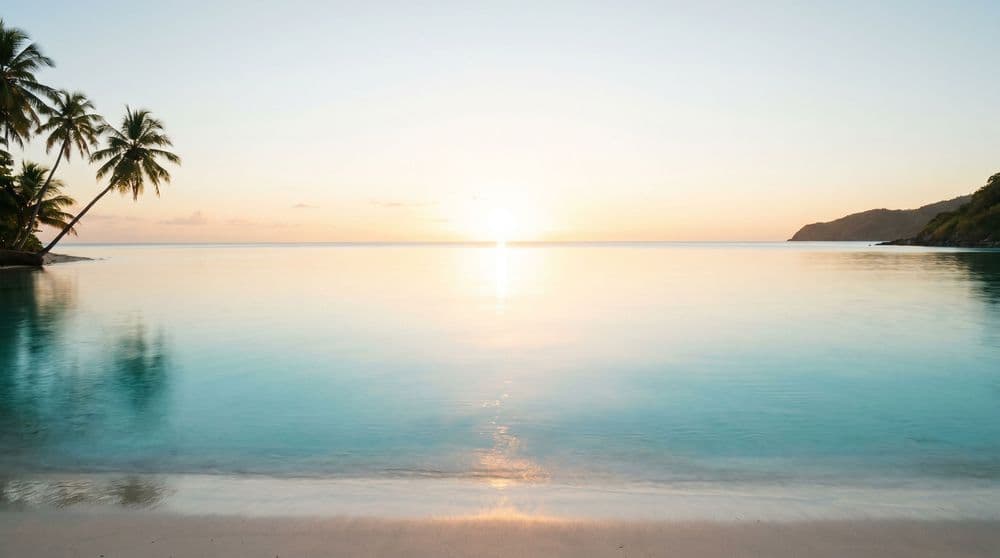 Low golden-hour sun just above the open sea horizon over a calm, glassy turquoise Koh Samui bay, coconut palms leaning from the left and a distant headland to the right.