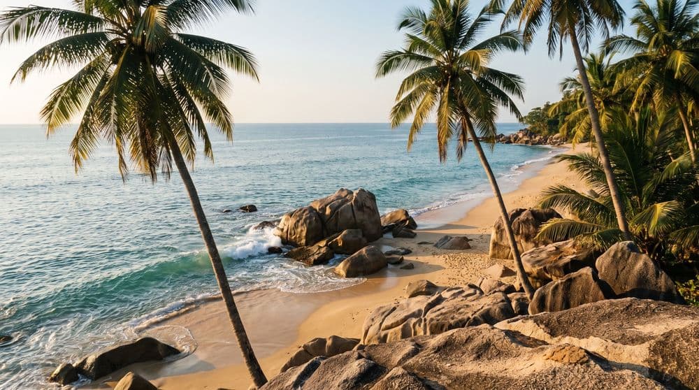 Weathered granite boulders meeting golden sand at the end of a quiet Koh Samui beach at golden hour, turquoise surf curling around the rocks