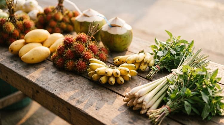 Tropical fruit, drinking coconuts and Thai herbs laid out on a rustic wooden market table in warm early-morning light