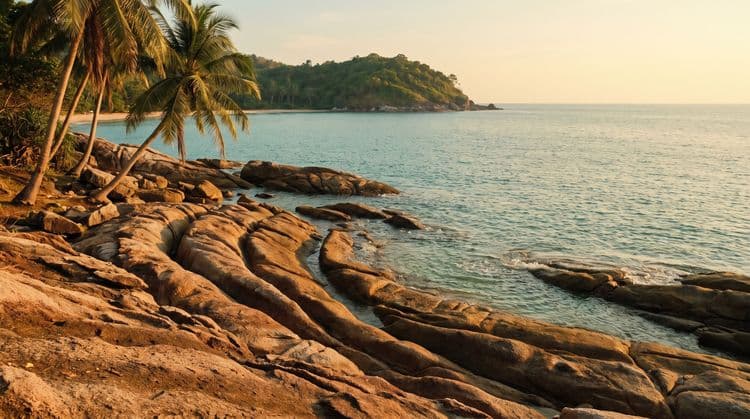 Sun-warmed reddish stone rock formation at the water edge on Koh Samui, golden hour