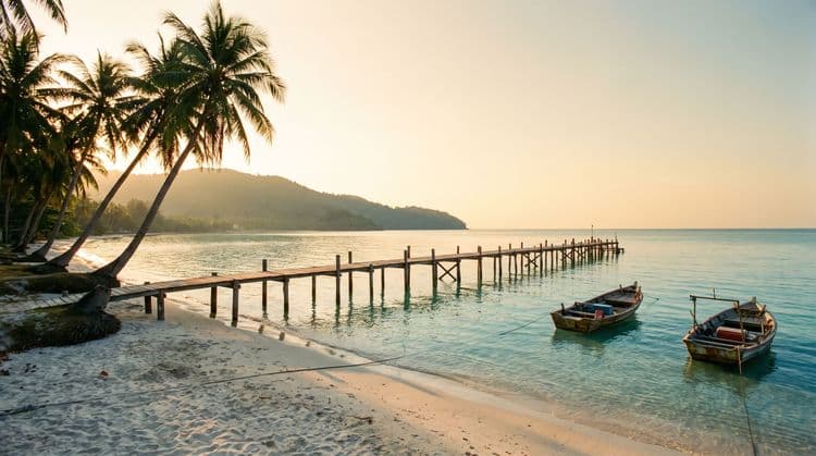 Wooden jetty at golden hour with fishing boats moored in calm shallow water, Koh Samui