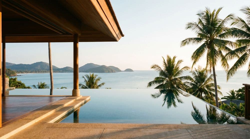 Golden-hour view from a covered villa terrace over an infinity pool toward a calm Koh Samui bay and palms