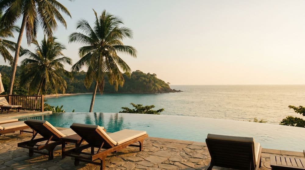 Golden-hour infinity pool edge on a private villa terrace overlooking a calm bay and green headland